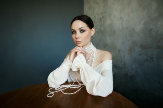 Girl dressed in white boho clothing with white pearl beads around her neck is sitting